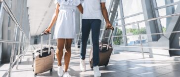 A couple walking through their terminal at an airport in sneakers and easy-to-wear travel outfits.