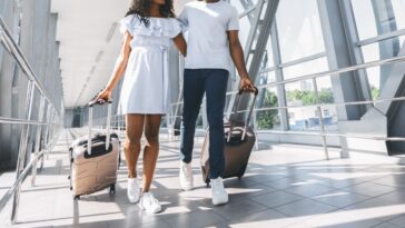 A couple walking through their terminal at an airport in sneakers and easy-to-wear travel outfits.